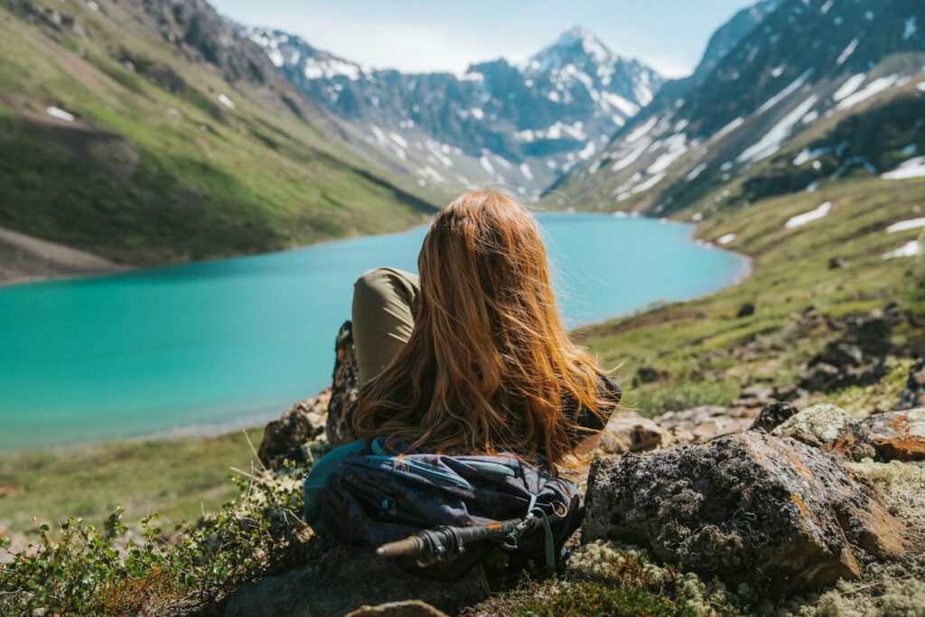 a woman sitting on a rock looking at a lake