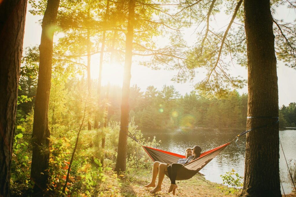 man and woman seating on gray hammock beside trees during daytime